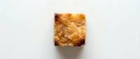 Freshly baked square shortbread cookie with golden-brown crumbly texture and caramelized edges on white background for food photography and baking content.
