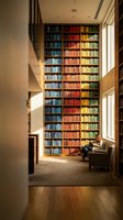 Modern home library with floor-to-ceiling rainbow bookshelf and reading nook. Contemporary interior design with organized colorful books and natural lighting.