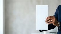 Close-up of male hand holding blank white card or paper against neutral background, suitable for business presentations, marketing mockups, and corporate advertising campaigns.