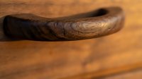 Rustic handcrafted wooden drawer handle with rich dark grain texture on warm oak surface, showcasing artisan woodworking and natural material detail.