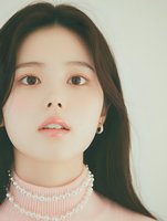 Young Asian woman with natural makeup wearing pink pearl choker necklace and small earrings against light background, soft dreamy portrait lighting.