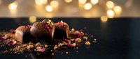 Chocolate truffles dusted with cocoa and crushed berries on dark surface with warm bokeh lights, perfect for dessert and confectionery designs.