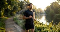 Young athletic Caucasian man jogging along scenic river path during golden hour sunrise workout session for healthy lifestyle and fitness motivation.