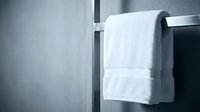 White towels hanging on a black metal rail against a gray textured wall in a modern bathroom setting for spa and wellness design projects.