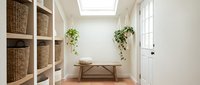 Bright modern entryway with wooden bench, wicker storage baskets, hanging plants and natural light from skylight creating welcoming home interior space.
