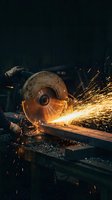 Industrial worker using angle grinder cutting metal with bright orange sparks flying in dark workshop atmosphere for manufacturing projects.