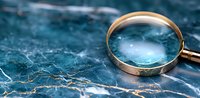 Golden magnifying glass on blue marble surface with natural veining pattern creates dramatic investigative mood for business and detective concepts.