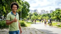 Young man with curly dark hair and medium brown skin tone jogging in urban park with city skyline, wearing yellow-green athletic shirt, for fitness and wellness content.