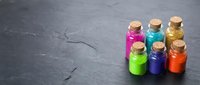 Colorful liquid-filled glass bottles with cork stoppers arranged on dark slate surface, suitable for cosmetics, essential oils, potions, or craft projects.