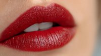 Close-up of woman's lips wearing glossy red lipstick with smooth texture, showcasing makeup artistry and cosmetic application for beauty campaigns.