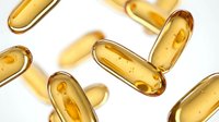 Golden vitamin capsules scattered on white background for health and wellness supplement advertising and pharmaceutical marketing materials.