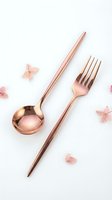 Rose gold cutlery set with spoon and fork on white background, decorated with delicate pink flowers, elegant flatware for modern table setting.