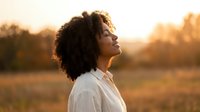 Young African American woman with curly hair enjoying peaceful moment outdoors during golden hour sunset, eyes closed in meditation and gratitude.