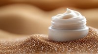 Luxurious face cream jar nestled in shimmering golden sand particles with soft focus effect, showcasing skincare product in spa wellness setting.