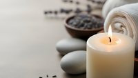Spa wellness setup with burning candle, smooth stones, towels and coffee beans creating peaceful relaxation atmosphere for massage therapy treatments.