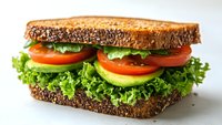 Fresh vegetable sandwich with crisp lettuce, sliced tomatoes and cucumbers between dark seeded bread slices on white background, ready for healthy lunch.