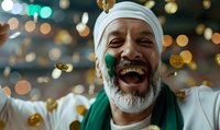 Joyful mature Middle Eastern man with gray beard wearing white turban and green scarf laughing heartily amid falling golden confetti and festive bokeh lights.
