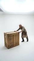 Senior Caucasian male craftsman in apron examining large wooden crate in minimalist white studio space for shipping and logistics concepts.