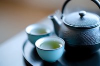 Traditional cast iron teapot with two light blue ceramic cups filled with fresh green tea on dark wooden table, serene Asian tea ceremony setting.