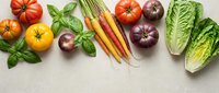 Fresh organic vegetables including heirloom tomatoes, colorful carrots, leafy greens and herbs arranged on neutral background for healthy cooking concepts.