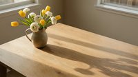 Ceramic vase with yellow tulips and white ranunculus on a wooden table in warm sunlight, casting soft shadows near a window.