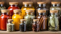 Colorful spice collection in glass jars with cork lids arranged on wooden shelf for cooking and culinary seasoning storage in kitchen pantry.