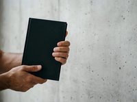 Male hands holding black notebook against concrete wall background for business, education, or publishing concepts.