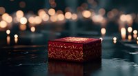 Ornate burgundy jewelry box with gold pattern on dark surface against blurred bokeh lights background, creating magical evening atmosphere.