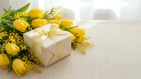 Yellow tulips and mimosa flowers with elegant gift box on light background for spring celebration and holiday greeting cards.