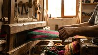 Traditional weaver working on wooden loom creating colorful textile in artisan workshop with natural lighting and authentic craftsmanship tools.