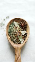 Wooden spoon filled with aromatic herbs and spices including star anise, bay leaves, and dried seasonings for cooking and culinary preparations.
