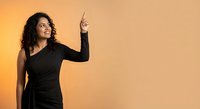 Young Hispanic woman in black dress pointing upward with finger against orange background, professional portrait for business and marketing materials.