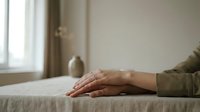 Calm female hands resting on a linen table in a minimalist interior with soft natural light and a ceramic vase in the background.