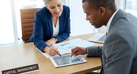 Professional business meeting with diverse executives analyzing financial reports and charts in modern office conference room.