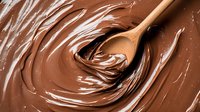 Swirling melted chocolate creates smooth spiral patterns with wooden spoon, macro shot showing rich texture and glossy surface for confectionery and dessert designs.
