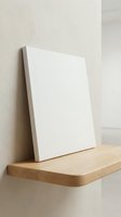 Blank white canvas on wooden shelf against neutral wall ready for artwork painting or creative projects in minimalist interior space.