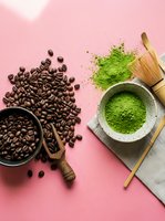 Coffee beans and matcha green tea powder with bamboo whisk on pink background. Healthy beverage ingredients for cafe menu and wellness lifestyle.