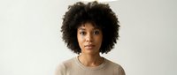 Young African American woman with natural curly afro hair wearing beige sweater against neutral background for lifestyle and fashion content.