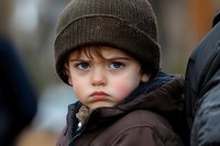 Serious young child wearing brown knit beanie and winter jacket with concerned expression outdoors in cold weather during winter season.