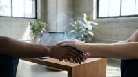 Business handshake between diverse professionals in modern office space with natural lighting and green plants creating partnership agreement atmosphere.