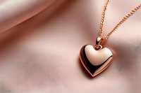 Rose gold heart pendant necklace on soft pink silk fabric background with gentle folds creating romantic mood and luxurious jewelry presentation.