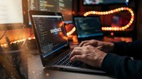 Professional developer coding on laptop in modern office with warm ambient lighting and bokeh effects creating productive workspace atmosphere.