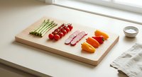 Fresh vegetables and sliced ham arranged on wooden cutting board in bright kitchen setting for healthy meal preparation and cooking concepts.