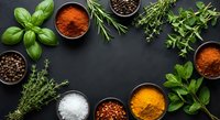 Fresh herbs and colorful spices arranged on dark slate background with copy space for culinary designs and cooking content.