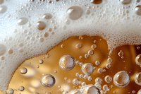 White foam bubbles and golden liquid macro photography showing refreshing beer texture with carbonation and frothy head against amber background.