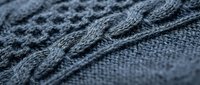 Gray knitted wool fabric with intricate cable pattern texture closeup for cozy winter fashion and textile design projects.