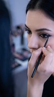 Young woman applying eyeliner makeup with precision brush in modern beauty salon mirror reflection for cosmetic tutorials and beauty routines.