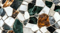 Decorative mosaic pattern with irregular pieces in green, white, and amber marble creating abstract geometric design. Natural stone texture background.