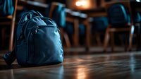Blue backpack sitting on wooden floor in modern office or classroom setting with chairs and warm lighting in background.