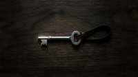 Antique silver key with ornate handle resting on dark wooden surface, symbolizing security, access, and mystery for design projects.